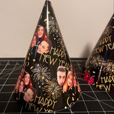 a black party hat with gold text reading happy new year, fireworks and peoples faces
